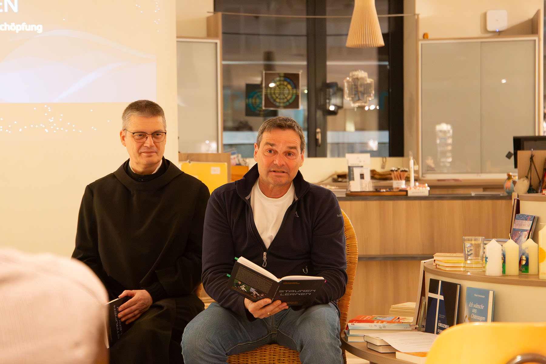 Mann im Habit sitze neben Mann, der aus einem Buch vorliest