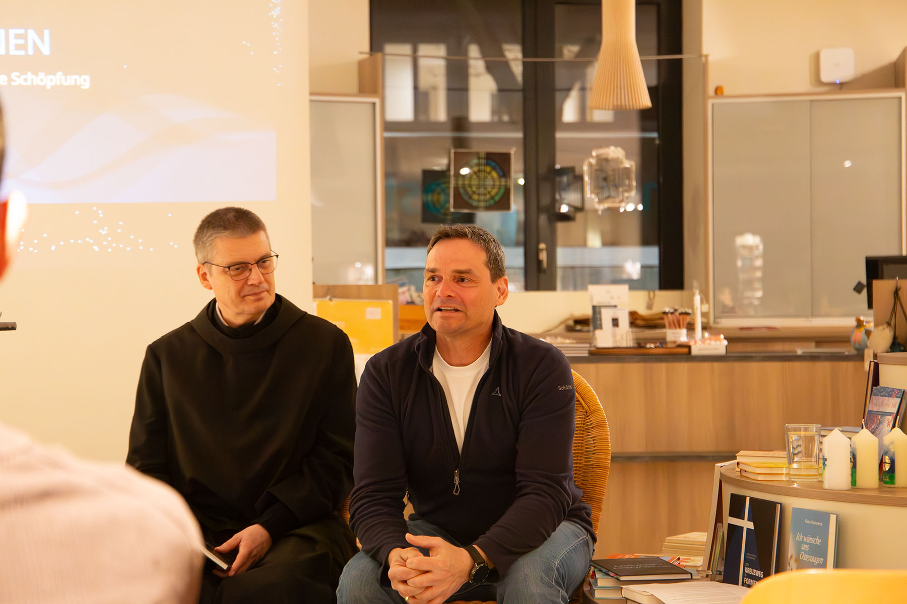 Mann im Habit und Mann in Alltagskleidung sitzen nebeneinander